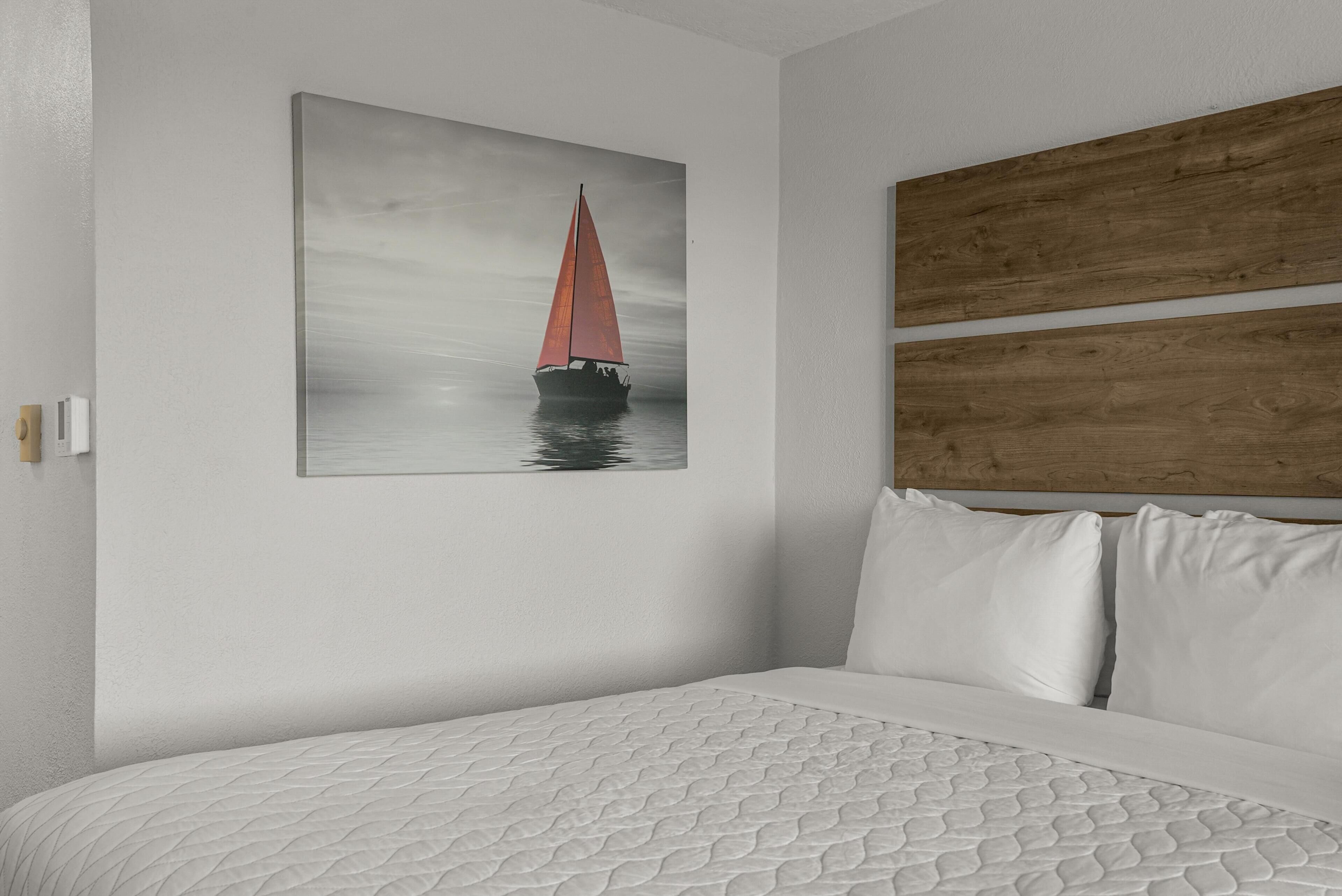 A bedroom with a bed, a wooden headboard, a white wall, and a painting of a sailboat.