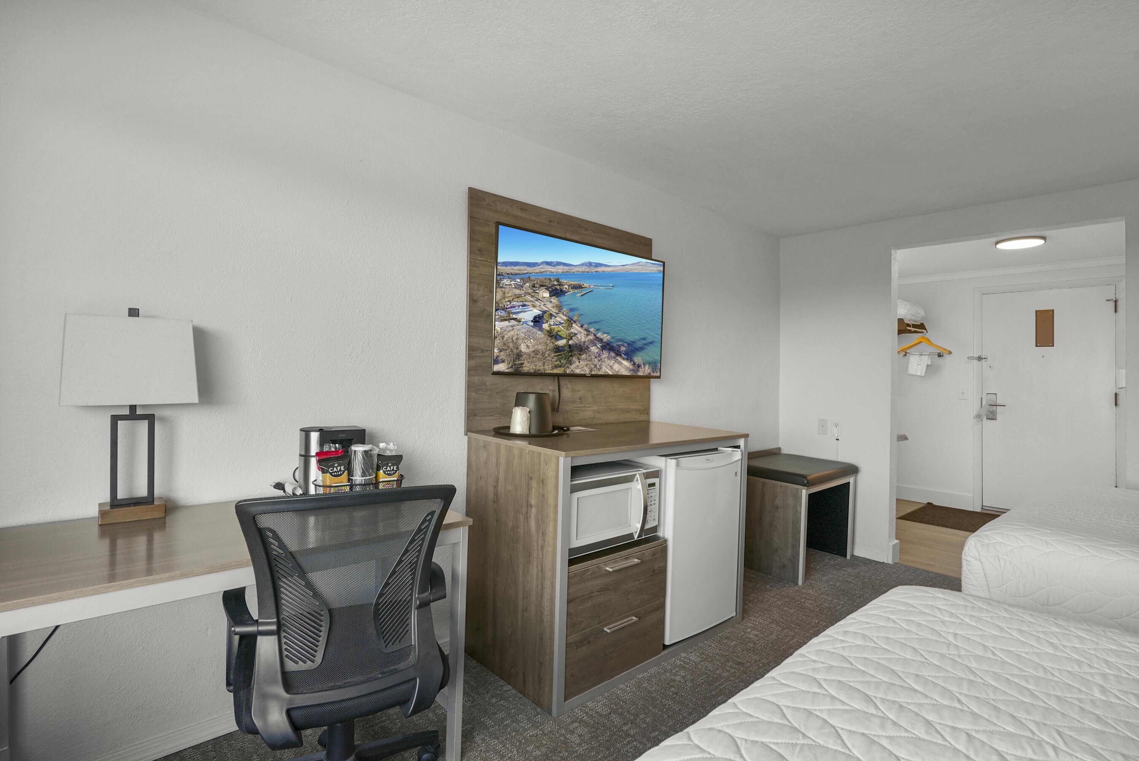 Une chambre d’hôtel équipée d’un bureau, d’une chaise, d’un lit, d’un four à micro-ondes et offrant une vue sur un paysage côtier.
