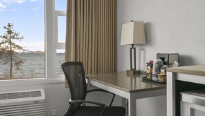 Hotellihuone, jossa on työpöytä, tuoli, lamppu, ilmastointilaite ja näkymä vesistöön.