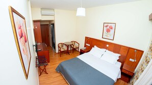 A hotel room with a bed, bedside tables, a desk with a chair, a small table with two chairs, and a painting on the wall. - Hotel Ena - Stylish Mountain View Suite With Pool (Lamia)