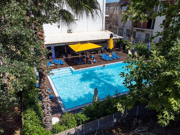 A rooftop pool with blue water, surrounded by lounge chairs and umbrellas, with buildings in the background.