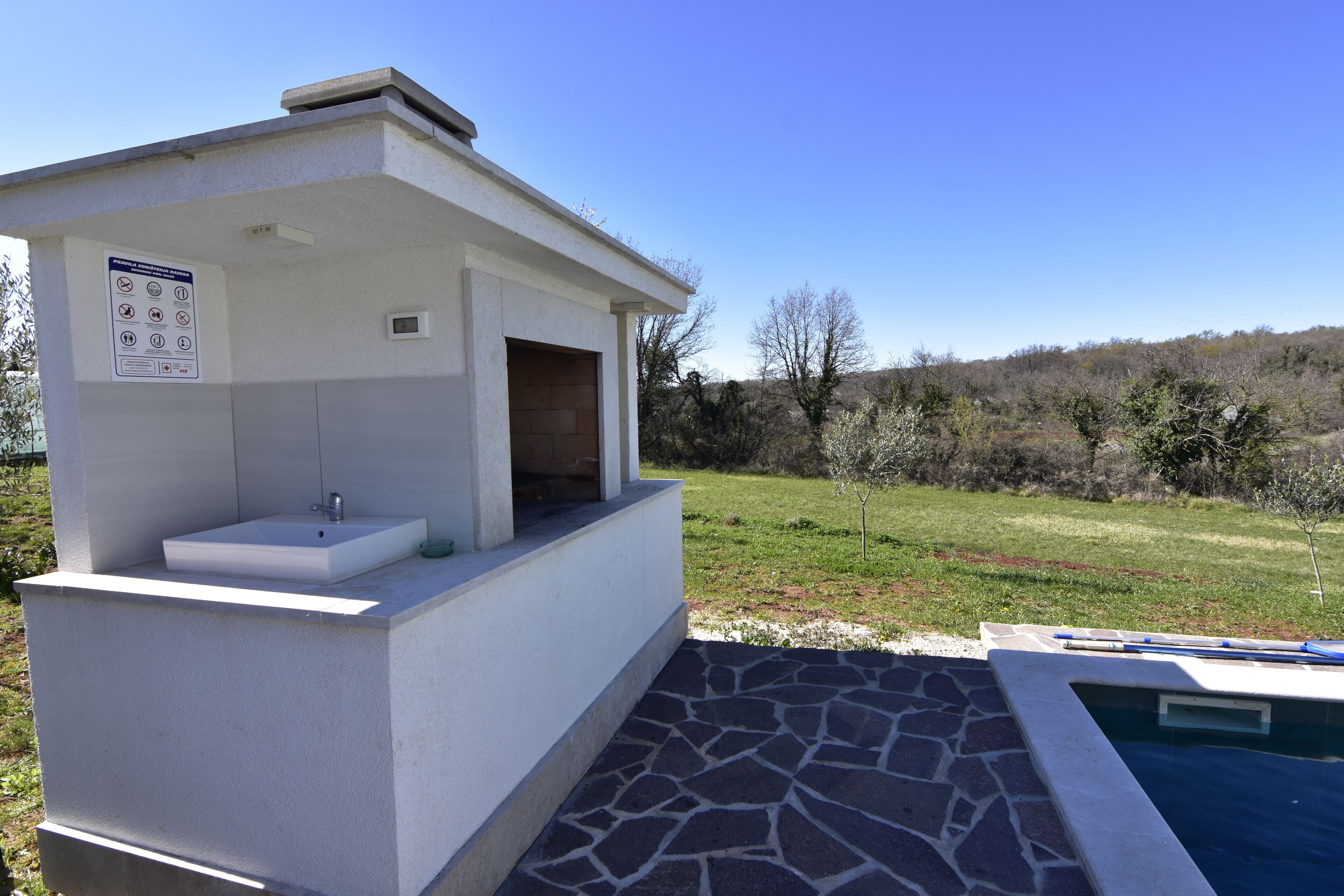 A small outdoor structure with a sink and a sign, adjacent to a swimming pool.