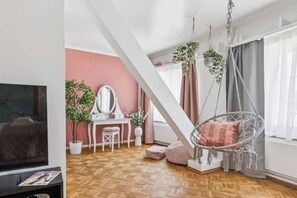 Ein modernes Wohnzimmer mit Holzboden, Fernseher, Schreibtisch mit Spiegel, Hängekorbsessel und Topfpflanzen.
