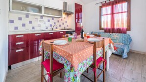 Une cuisine compacte avec un coin repas, comprenant une table dressée pour deux personnes, un meuble rouge et une fenêtre avec des rideaux.