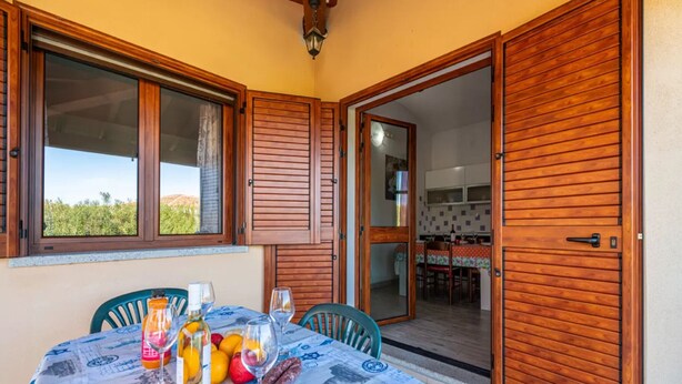 Un coin repas avec une table dressée pour deux personnes, une bouteille de vin et un panier de fruits.