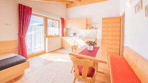 Quarto com cama, mesa de jantar com cadeiras, cozinha e porta de vidro corria para uma varanda.