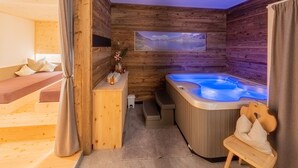 Interior de uma cabana de madeira com uma banheira de hidromassagem, um sofá e uma pequena mesa com um vaso.