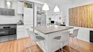 A modern kitchen with a central island, white cabinetry, and a colorful abstract wall art. - The Deck House Lorne (Lorne)