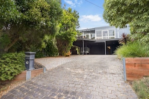 A modern house with a covered garage, paved driveway, and lush greenery. - The Deck House Lorne (Lorne)