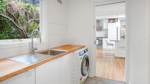 A modern kitchen with a wooden countertop, stainless steel sink, and a front-loading washing machine. - The Deck House Lorne (Lorne)