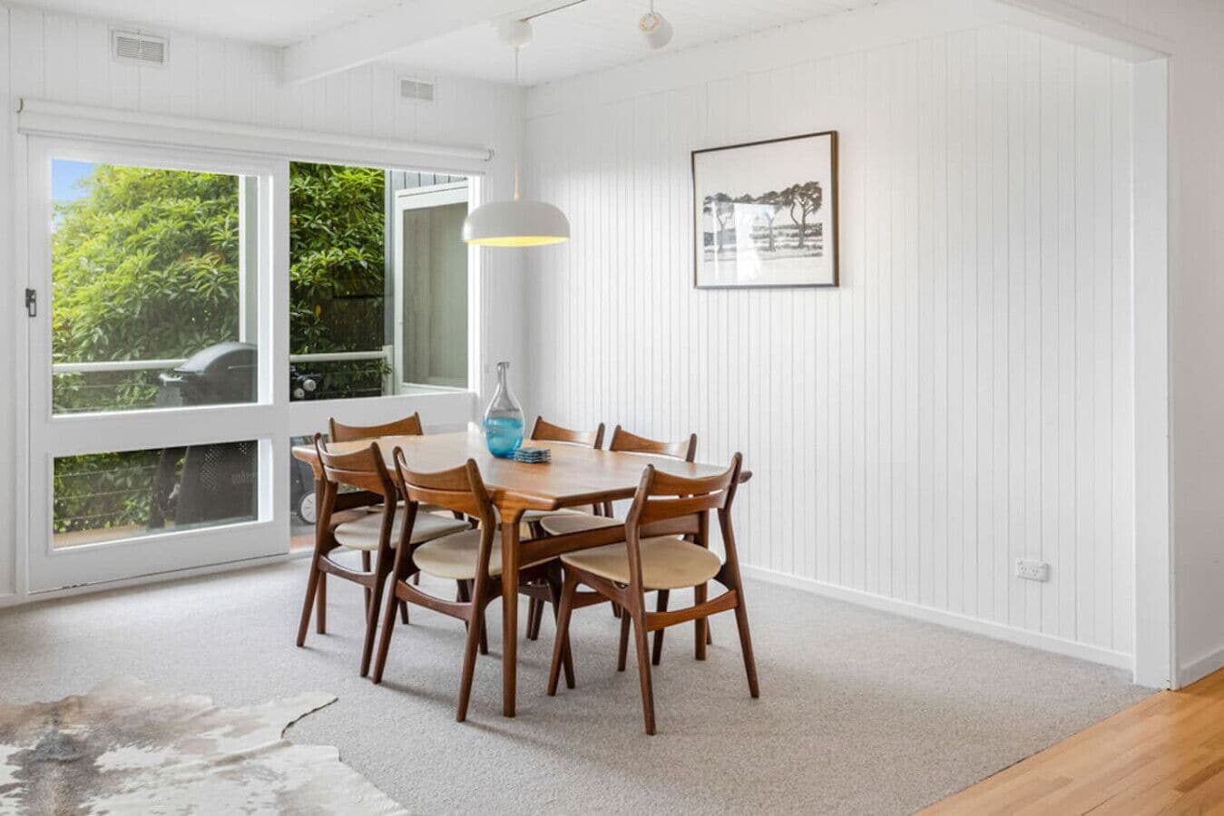 A dining area with a wooden table and chairs, a pendant light, and a framed picture on the wall.