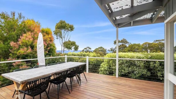 A wooden deck with a table and chairs, surrounded by lush greenery and a clear view of the sky. - The Deck House Lorne (Lorne)