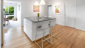 A modern kitchen with a central island, white cabinetry, and a wooden floor. - The Deck House Lorne (Lorne)