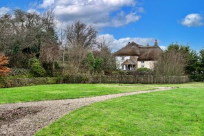 A thatched-roof house with a stone wall and a grassy yard.