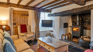 Een gezellige woonkamer met een stenen openhaard, houten balken, een televisie en comfortabele zithoek.
