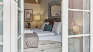 A hotel room with a bed, a bedside table, a lamp, and a mirror on the wall. - Old Town Riverside | AC | Balcony | Free Parking | Water View (Zürich)