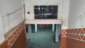 Un pasillo estrecho con suelo de rejilla metálica, paredes de azulejos y una ventana con reja.
