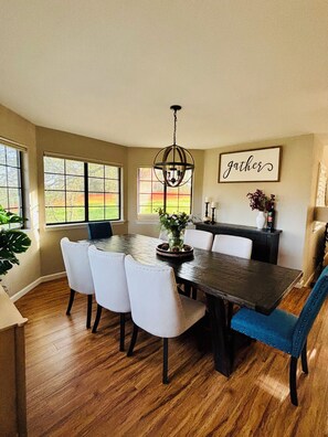 A dining area with a dark wooden table, white upholstered chairs, and a chandelier. - Perfect 4-bedroom house near lakes and trails in Folsom (Folsom)
