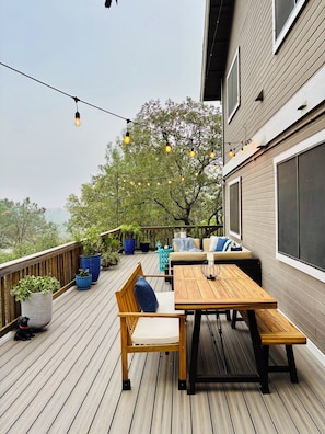 Une terrasse en bois avec une table et des chaises, des plantes en pot et des guirlandes lumineuses.