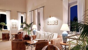 Un amplio salón con sillones de cuero, un sofá blanco y una mesita de centro. Hay plantas en macetas y una lámpara sobre una mesita auxiliar.