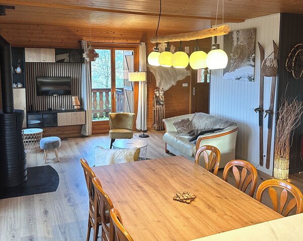 A cozy cabin interior with a wooden dining table, chairs, a sofa, a TV, and a fireplace.
