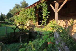 A rustic stone building with a wooden porch and a water wheel.