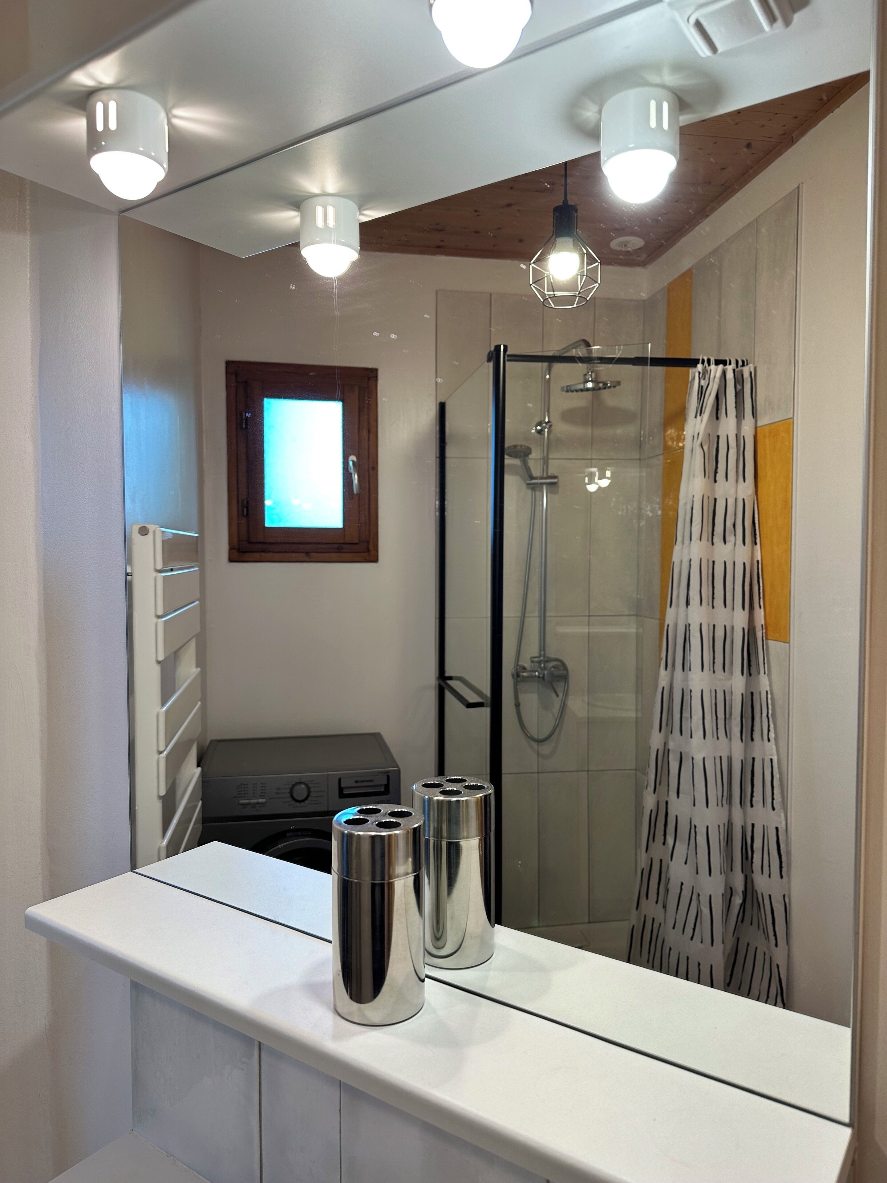 A modern bathroom with a shower, a mirror, and a countertop with two metallic containers.