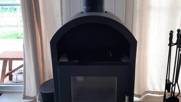 A black wood stove with a glass door, labeled "JUSTUS," in a room with a glass door and a view of a wooden deck outside.
