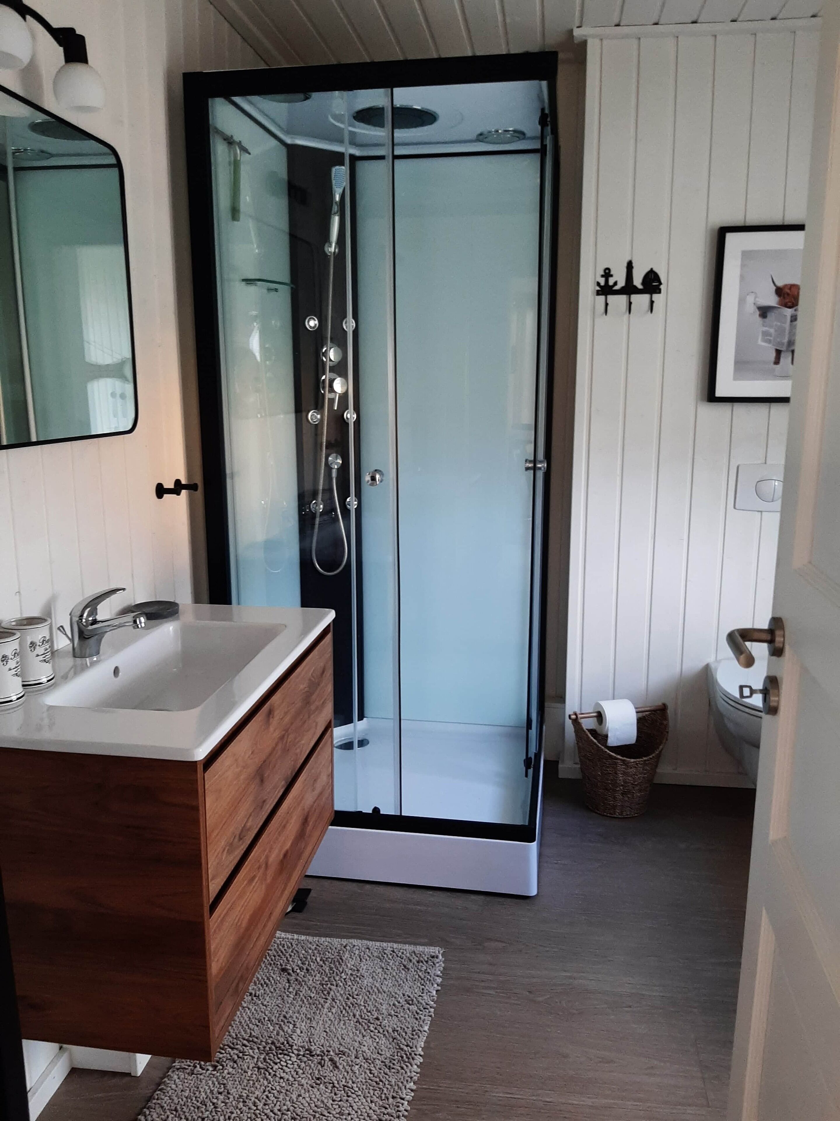 A modern bathroom with a glass-enclosed shower, a wooden vanity with a sink, and a framed picture on the wall.