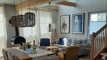 A cozy living room with a wooden dining table, chairs, a sofa, and a staircase.