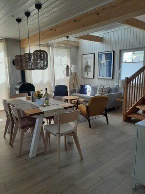 Een gezellige woonkamer met een houten eettafel, stoelen, een bank en een trap.