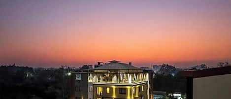 A multi-story building with illuminated windows, surrounded by greenery, during twilight.