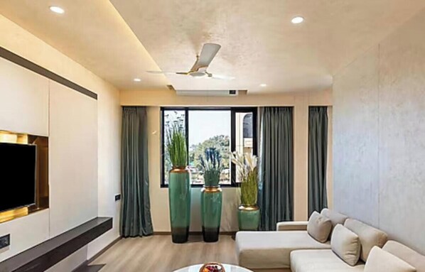 Una sala de estar moderna con una televisión de pantalla plana, un ventilador de techo, un sofá y ventanas amplias con cortinas.