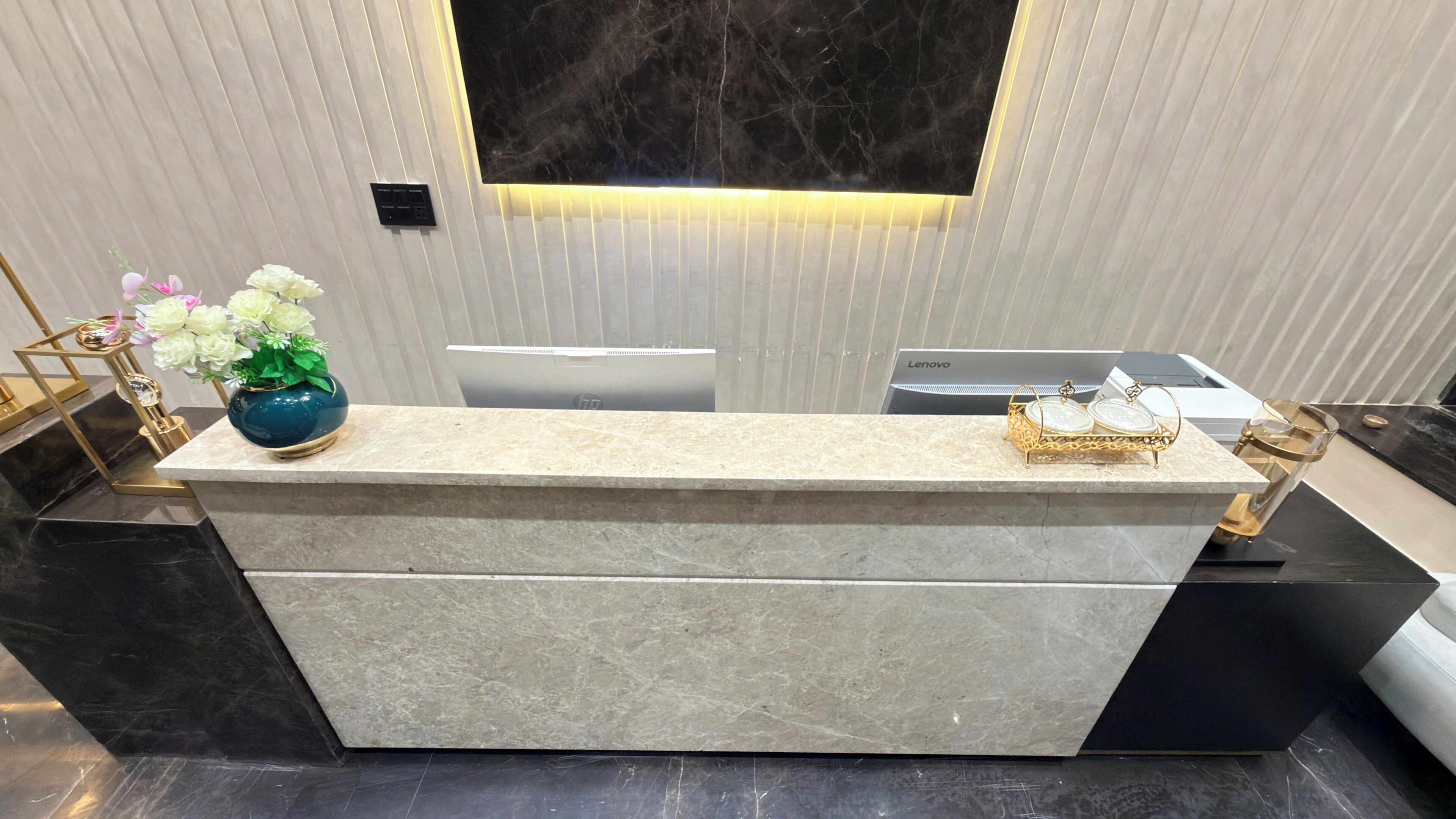 A reception desk with a marble top, a vase of flowers, and a laptop on it.