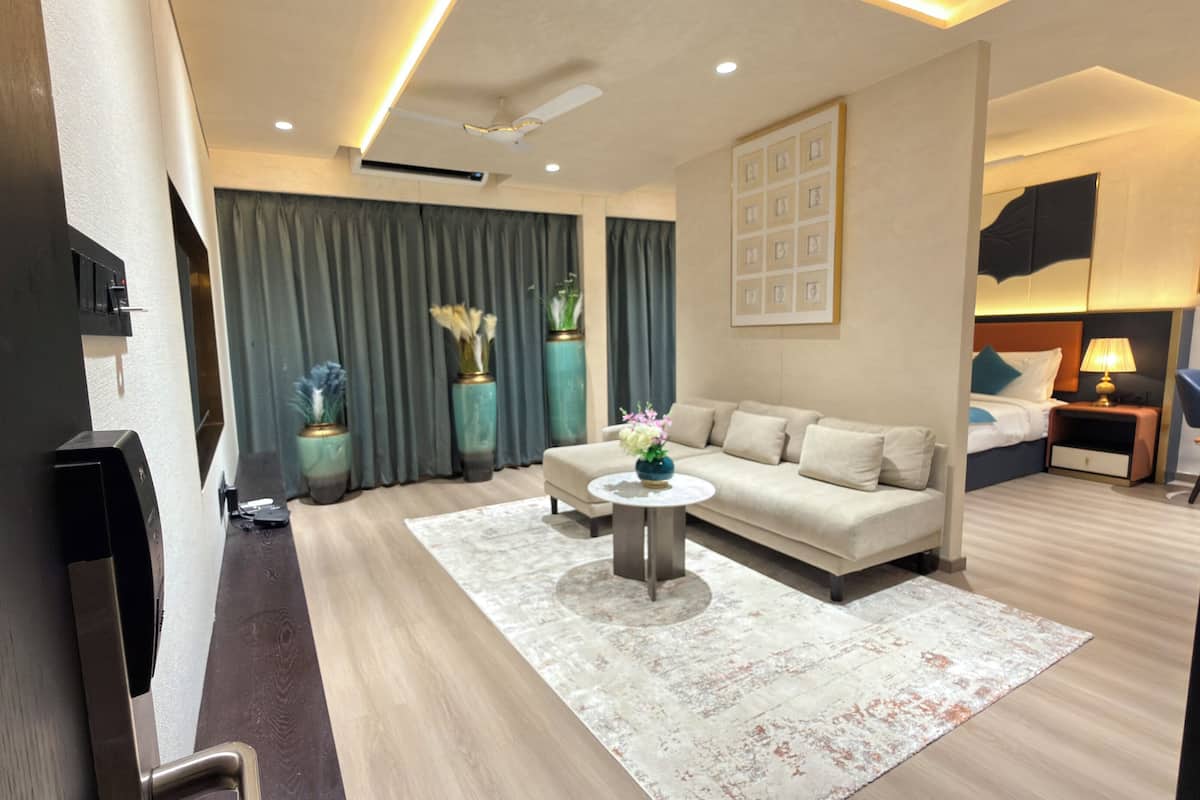 Una habitación de hotel moderna con sofá, una mesa de centro, televisor, cama, mesita de noche y una pared decorada con cuadros.