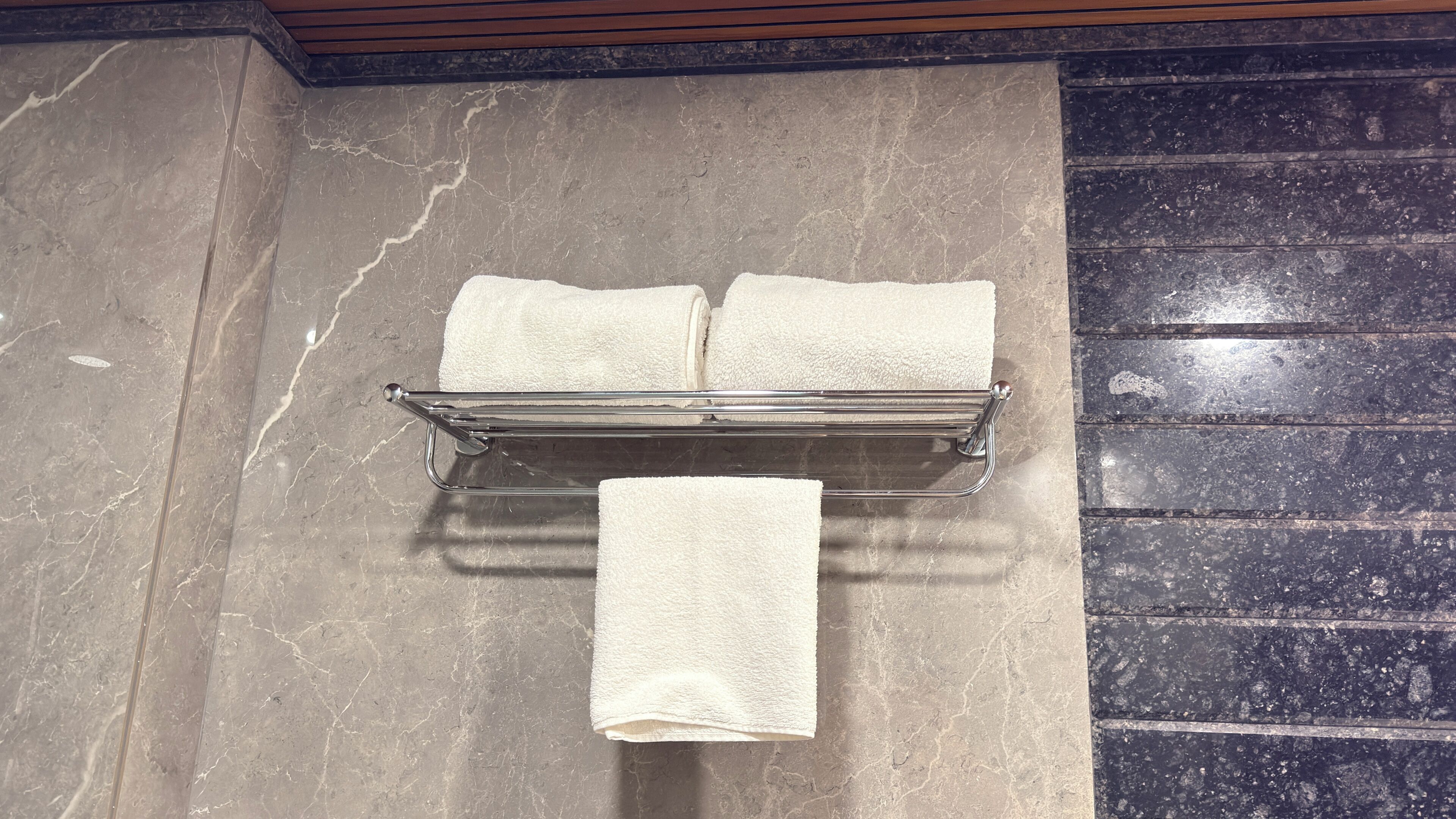 Un baño con pared de mármol, un perchero con tres toallas y techo de madera.