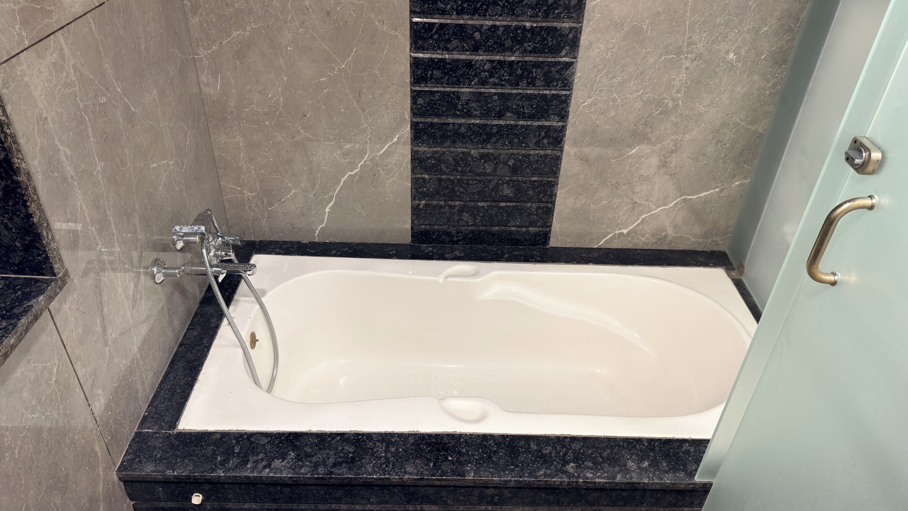 Una bañera con cabezal de ducha, encimera de mármol negro y un picaporte.