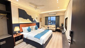 A hotel room with a bed, bedside table, lamp, sofa, TV, and a large window.