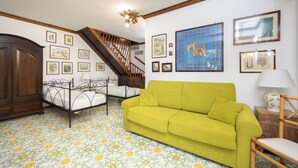 Ein Zimmer mit einem grünen Sofa, einem Bett mit Metallgestell, einem Holzschrank, einer Treppe und einem gemusterten Boden.