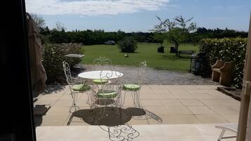 Een terras met een ronde tafel en stoelen, uitzicht op een gazon en een auto in de verte.