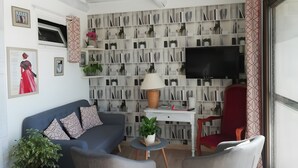 Un salon avec un canapé, des fauteuils, un téléviseur, une bibliothèque et une fenêtre.