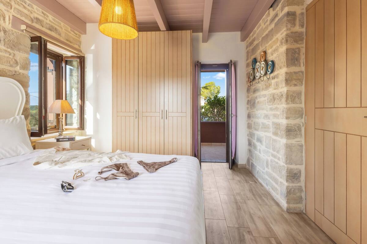 A bedroom with a bed, a nightstand, a lamp, a wardrobe, and a view through a door.