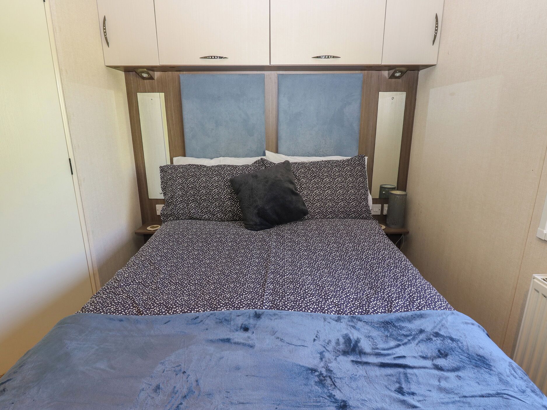 Un lit avec une couvre-lit à motifs, deux oreillers, une couverture bleue et une tête de lit en bois agrémentée d’un miroir.