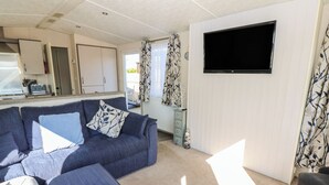 Uma sala de estar com sofá, apoio para os pés e uma TV de tela plana na parede.