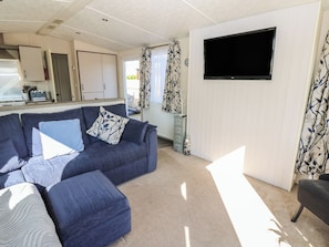 A living area with a sofa, ottoman, and a flat-screen TV mounted on the wall. - Plot 42 (Carlisle)