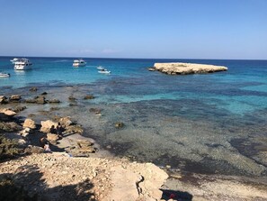 Eine felsige Küstenlinie mit klarem, blauem Wasser, Booten und einer kleinen Insel.