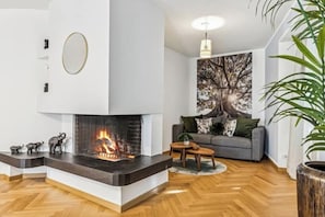 A modern living room with a fireplace, a grey sofa, and a large tree painting on the wall.