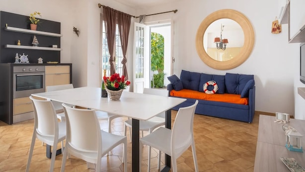 A modern kitchen with a dining table and chairs, a blue sofa with an orange cushion, and a round mirror on the wall. - Villa Solaria - Giardino Privato and Aria Condizionata (Porto Cesareo)