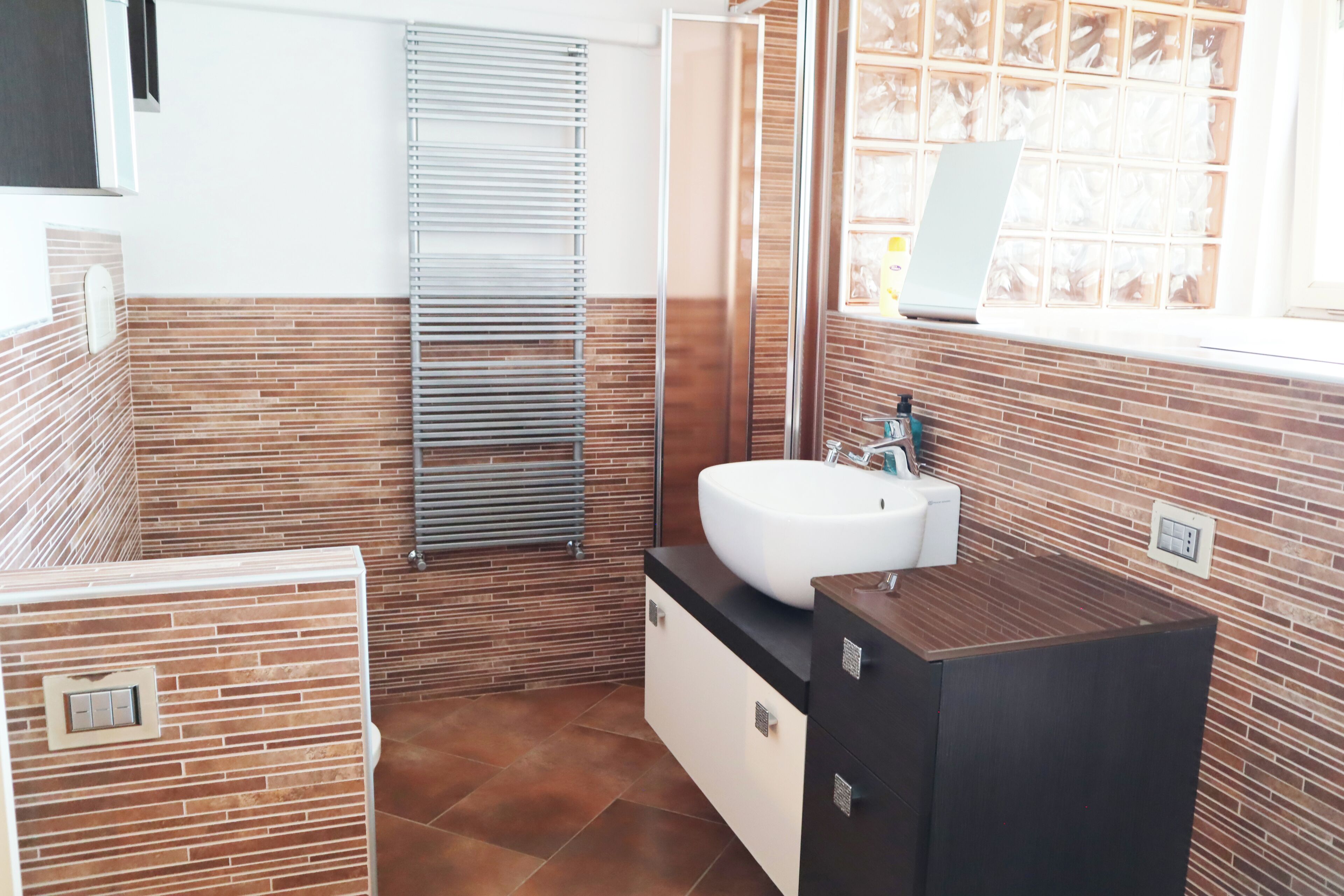 Ein Badezimmer mit einem weißen Waschbecken, einem Spiegel und einem Fenster mit Jalousien.