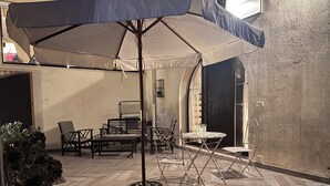 Un patio al aire libre con una mesa, sillas, una planta en maceta y un paraguas grande.